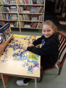 Dziewczynka układa puzzle przy stoliku w bibliotece
