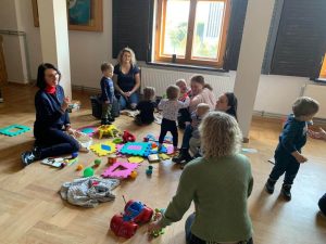 Dzieci siedzą na podłodze z mamami i panią dentystką wśród zabawek.