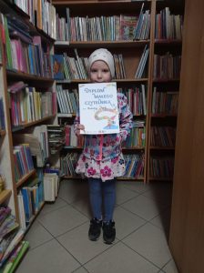 Dziewczynka z Dyplomem Małego Czytelnika stoi wśród regałów z książkami.