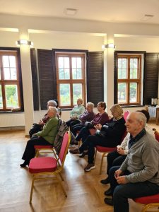 Seniorzy siedzą na krzesłach na dużej sali w bibliotece