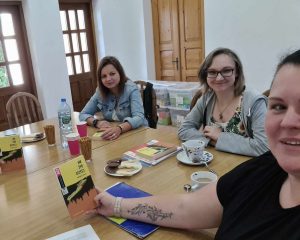 kobiety siedzą przy stole i rozmawiają o książce popijając herbatę i wodę.