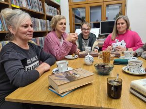 Grupa kobiet siedzi przy stole, przy herbacie, rozmawiają o książce
