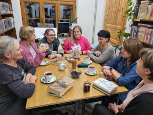 Grupa kobiet siedzi przy stole, przy herbacie, rozmawiają o książce