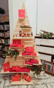 Półka w kształcie choinki stoi w wypożyczalni, są na niej przygotowane książki niespodzianki świąteczne do wypożyczania. 