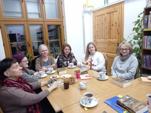 Grupa kobiet siedzi wokół stołu, rozmawiając na temat książki i popijając herbatę.