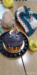 Tort urodzinowy leży na stole, a wokół niego robótki szydełkowe