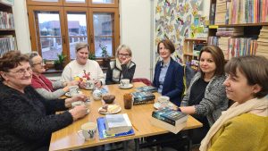 Grupa kobiet siedzi wokół stołu i rozmawia na temat książki przy herbacie. 