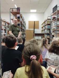 W bibliotece na krześle siedzi ość, który opowiada siedzącym przed nim dzieciom o owadach