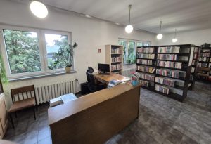 Wnętrze biblioteki w Mikołajowicach. Lada biblioteczna przy oknie, obok regały z książkami