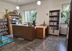 Wnętrze biblioteki w Mikołajowicach. Lada biblioteczna przy oknie, obok regały z książkami
