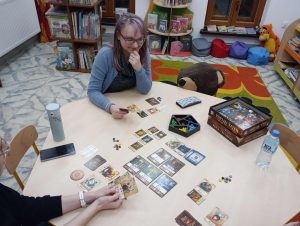 Przy stolikach kilka osób gra w gry planszowe i karciane.