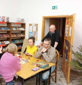 Przy stolikach kilka osób gra w gry planszowe i karciane.