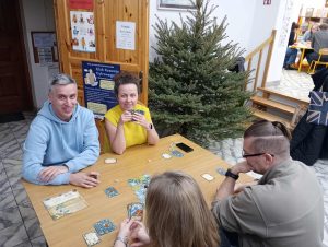 Przy stolikach kilka osób gra w gry planszowe i karciane.