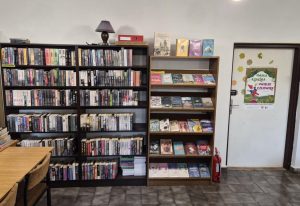 Dział kryminału. Pod ścianą stoją regał z książkami, po prawej stronie znajdują się drzwi wejściowe. Na regale stoi lampka nocna