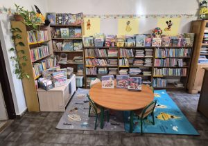 Dział dziecięcy biblioteki. Pod ścianami stoją regały z książkami, przed nimi stoliczek i krzesełka