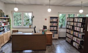 Wnętrze biblioteki w Mikołajowicach. Lada biblioteczna przy oknie, obok regały z książkami
