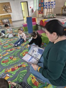 Bibliotekarka czyta dzieciom książkę. Dzieci siedzą na dywanie